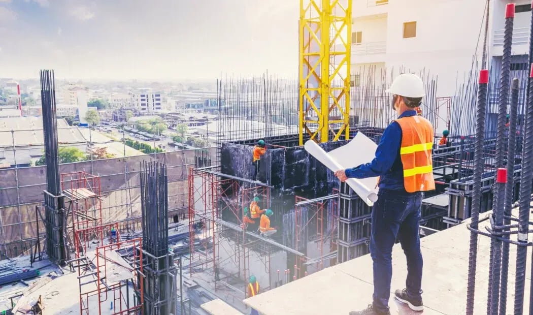 construction worker wearing PPE looking down on a construction site from a high ledge construction worker wearing PPE looking down on a construction site from a high ledge