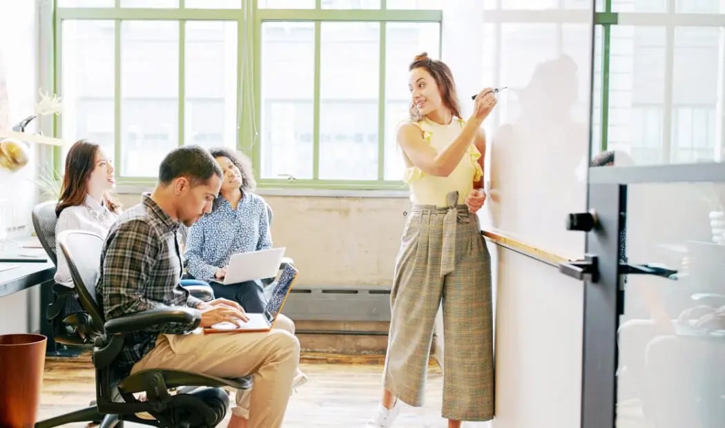 Financial services professionals typing while woman writes on whiteboard Financial services professionals typing while woman writes on whiteboard