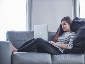Woman on sofa against large cushions working on a laptop on her lap