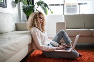 Woman sat on the floor working on a laptop on her leg