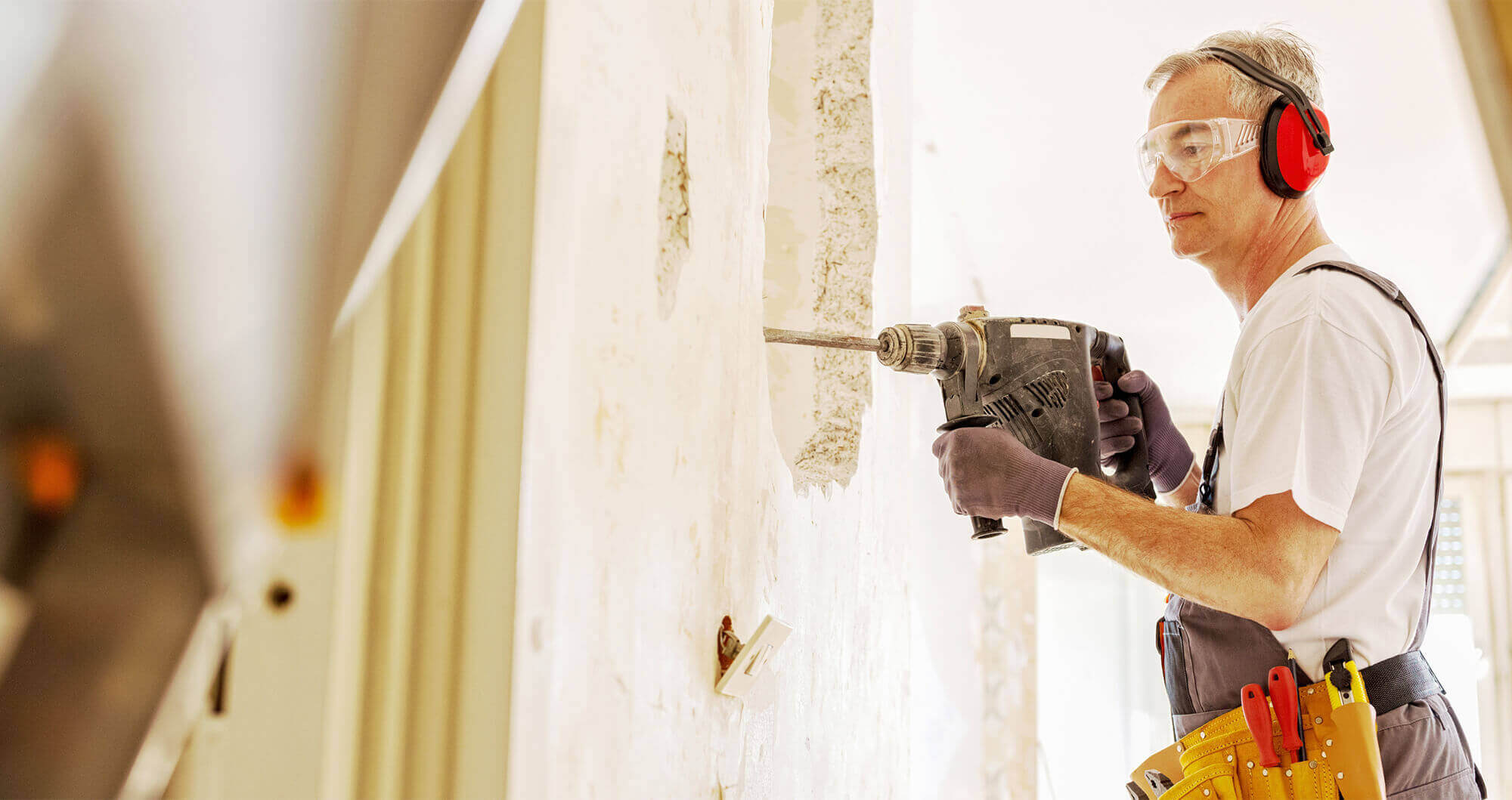construction worker wearing PPE drilling a wall