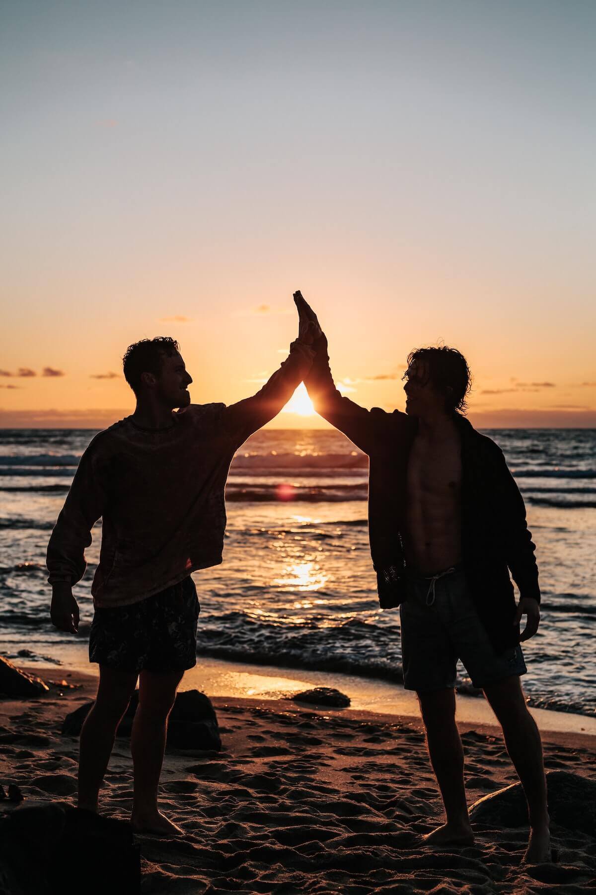 two men high fiving on the beach at sunset