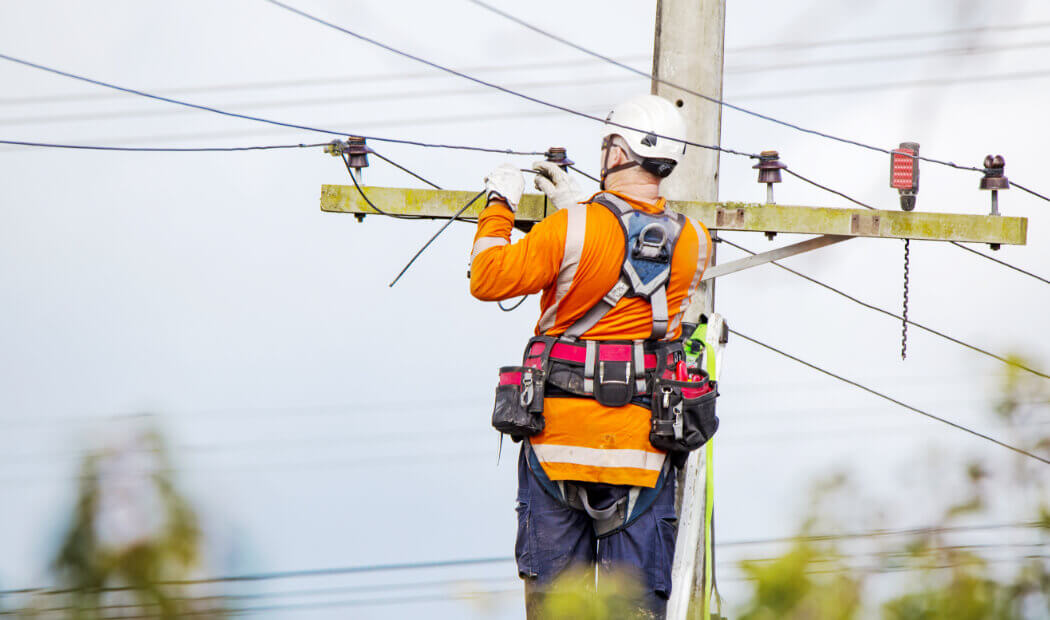 utilities worker wearing PPE and harness while working on cabling
