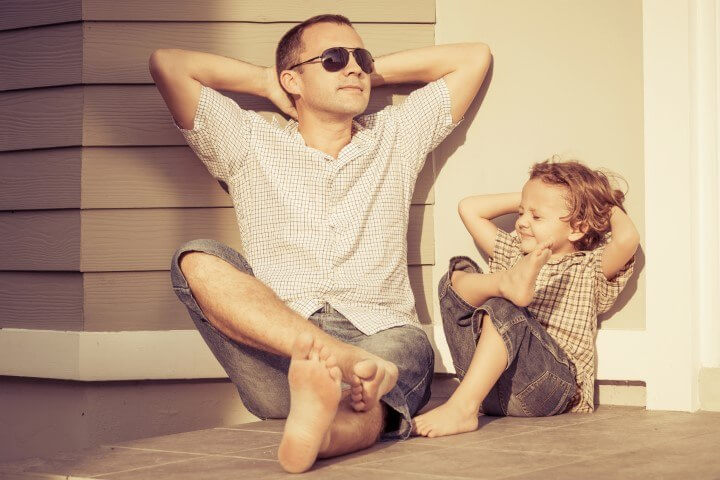 Father and young son sat on a porch with hands behind their heads