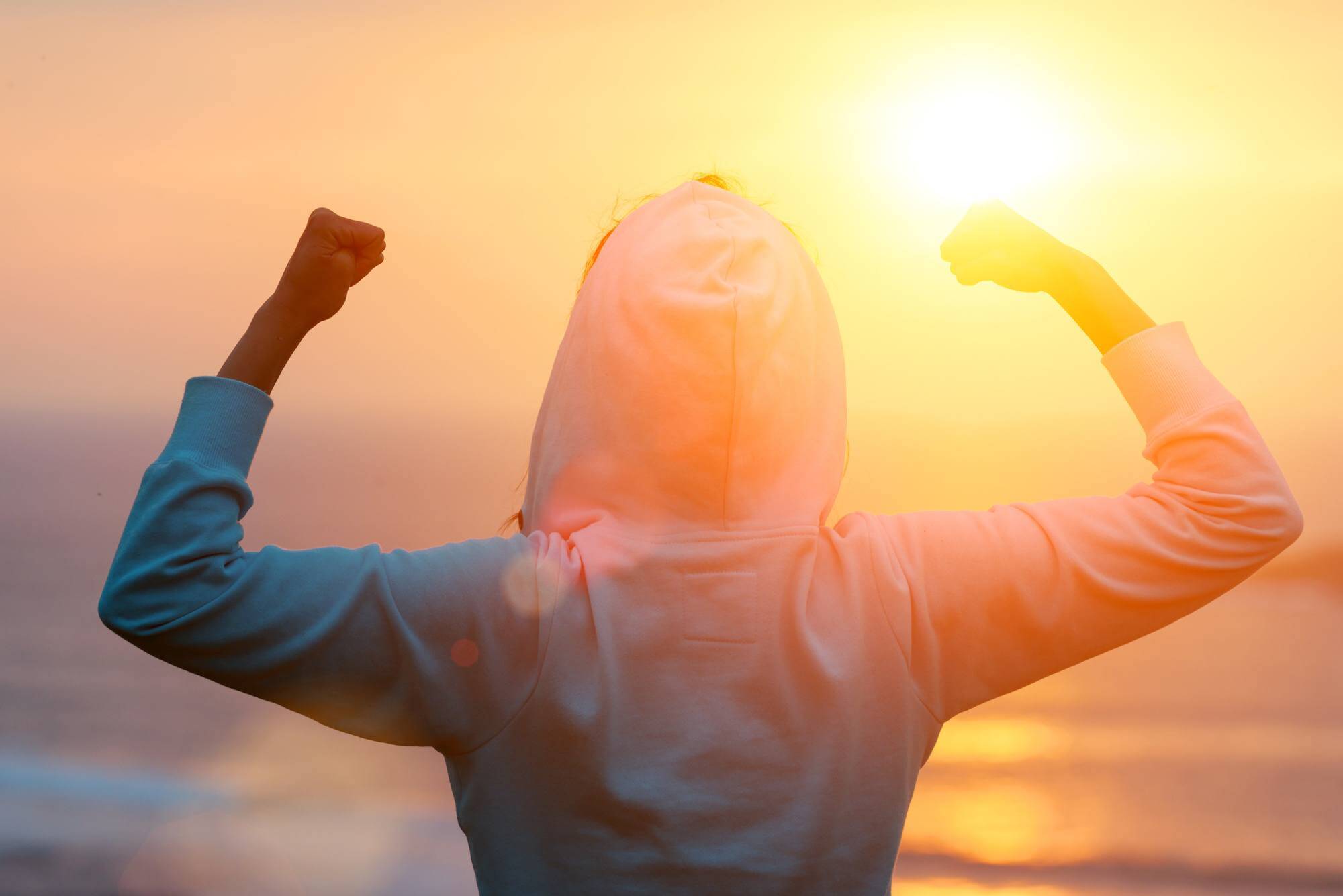 A person in a hoodie facing the sun flexing biceps