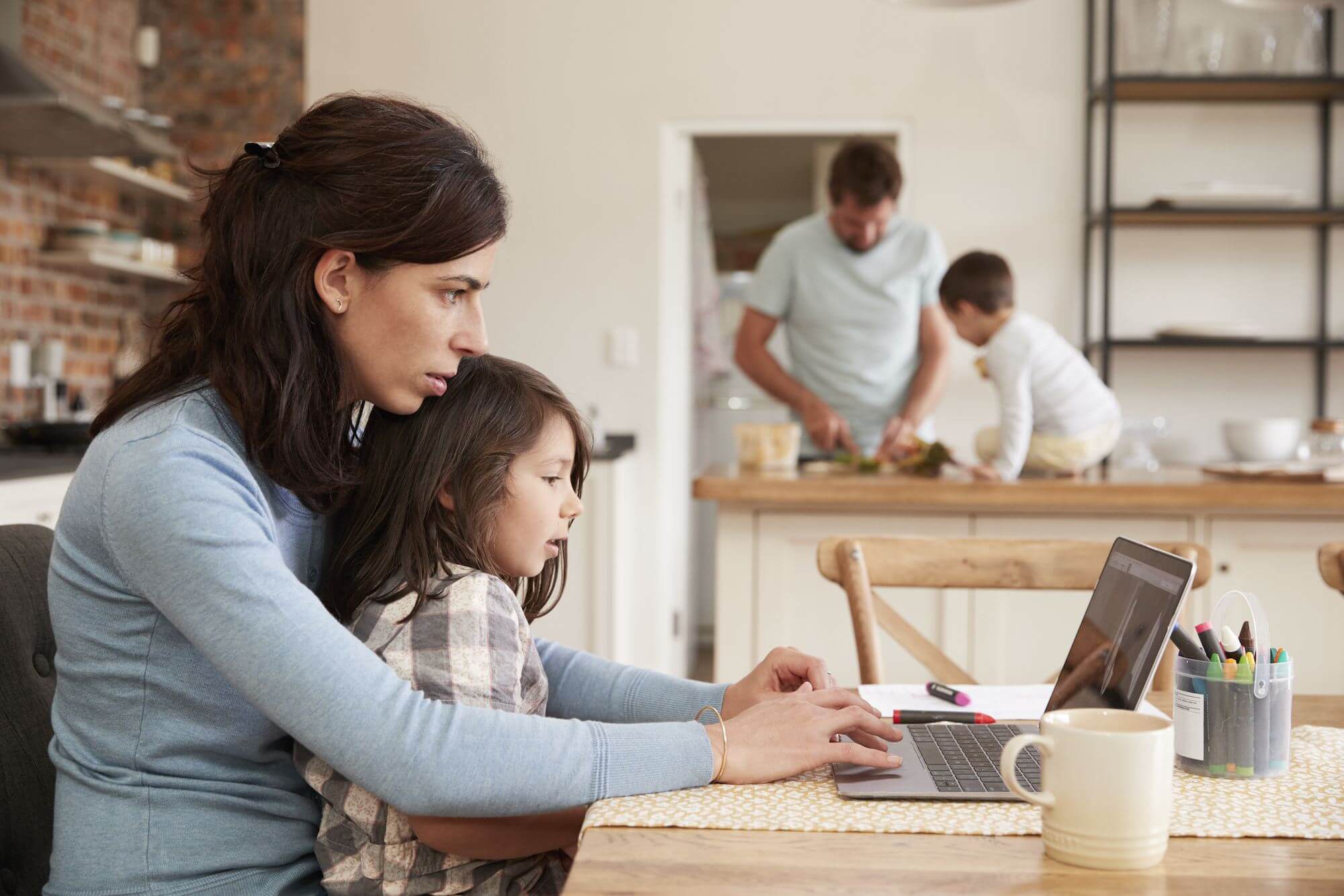mother and child at a laptop whilst father and child prepare food