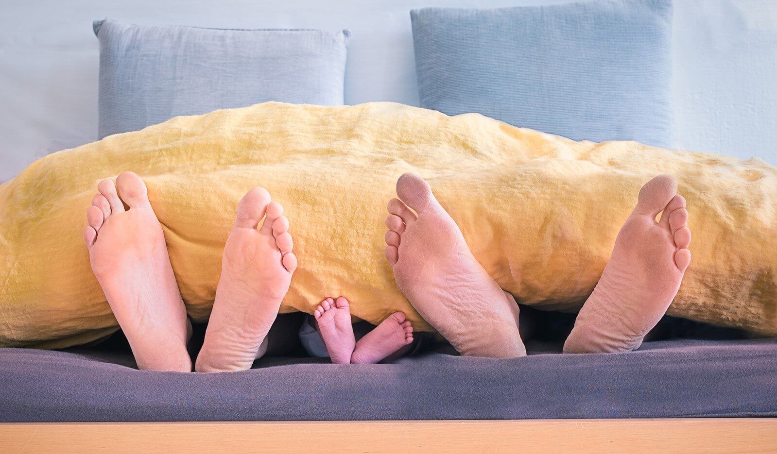 two pairs of adult feet and a small child's feet sticking out of duvet