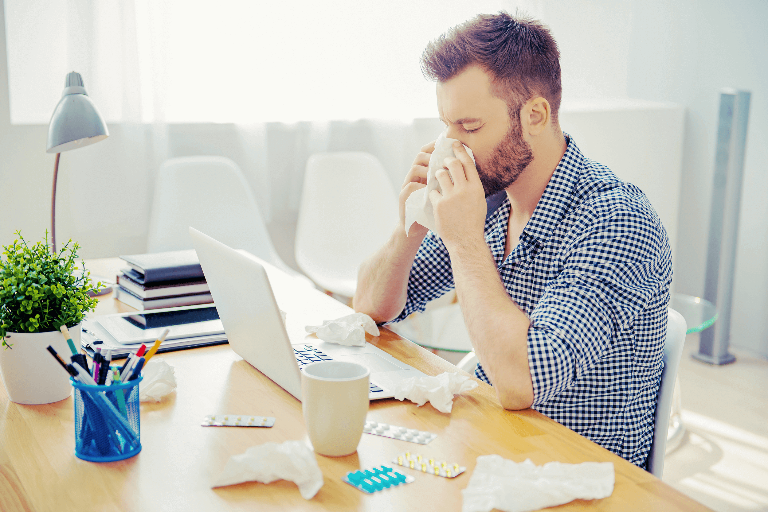 a man working on a laptop blowing his nose in to tissues